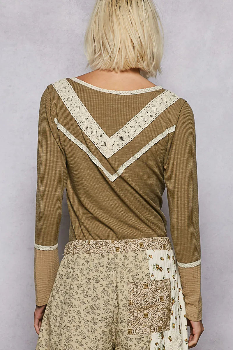 Back view of model in an olive rib knit top with cream lace trim on yoke paired with beige floral paisley pants on a clean background