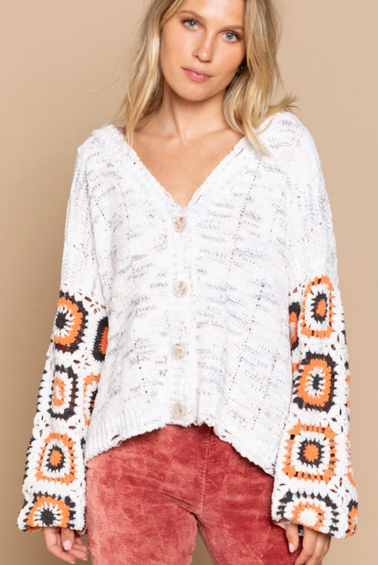 Ivory button-front cardigan with orange and black crochet granny-square sleeves and distressed hem for retro fall layering looks.