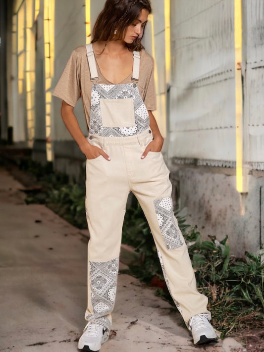 Cream denim overalls with paisley patchwork, frayed edges, adjustable straps, and pockets for a vintage-inspired casual look.