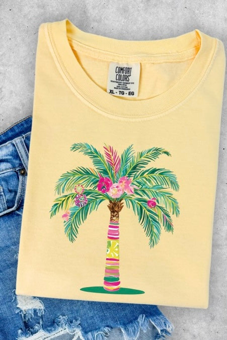 Coastal-inspired Comfort Colors yellow unisex t-shirt with vibrant palm tree and floral graphic in pink, green, and turquoise; styled with distressed denim shorts on a flat lay, evoking a carefree beachside vibe perfect for sun-chasers and laid-back tropical summer looks.