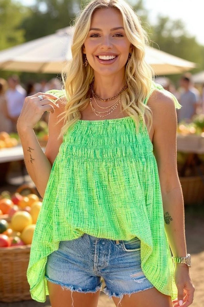 Green sleeveless top with denim shorts, gold jewelry, and tousled blonde hair—styled for summer at an outdoor market.