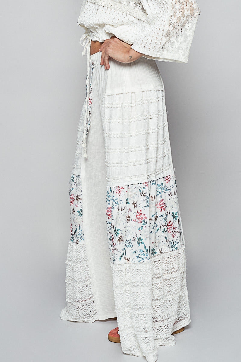Side studio view of Sunspell Flares, highlighting the elastic waistband, drawstring, side profile of the wide, flared leg, and floral lace patchwork.
