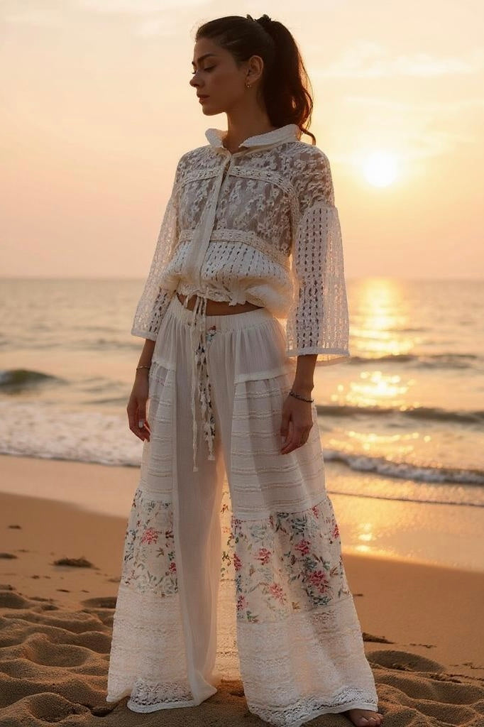 Woman with a ponytail standing on a beach at sunset, wearing a white sheer lace top and Sunspell Flares, showcasing the flared leg and patchwork details.