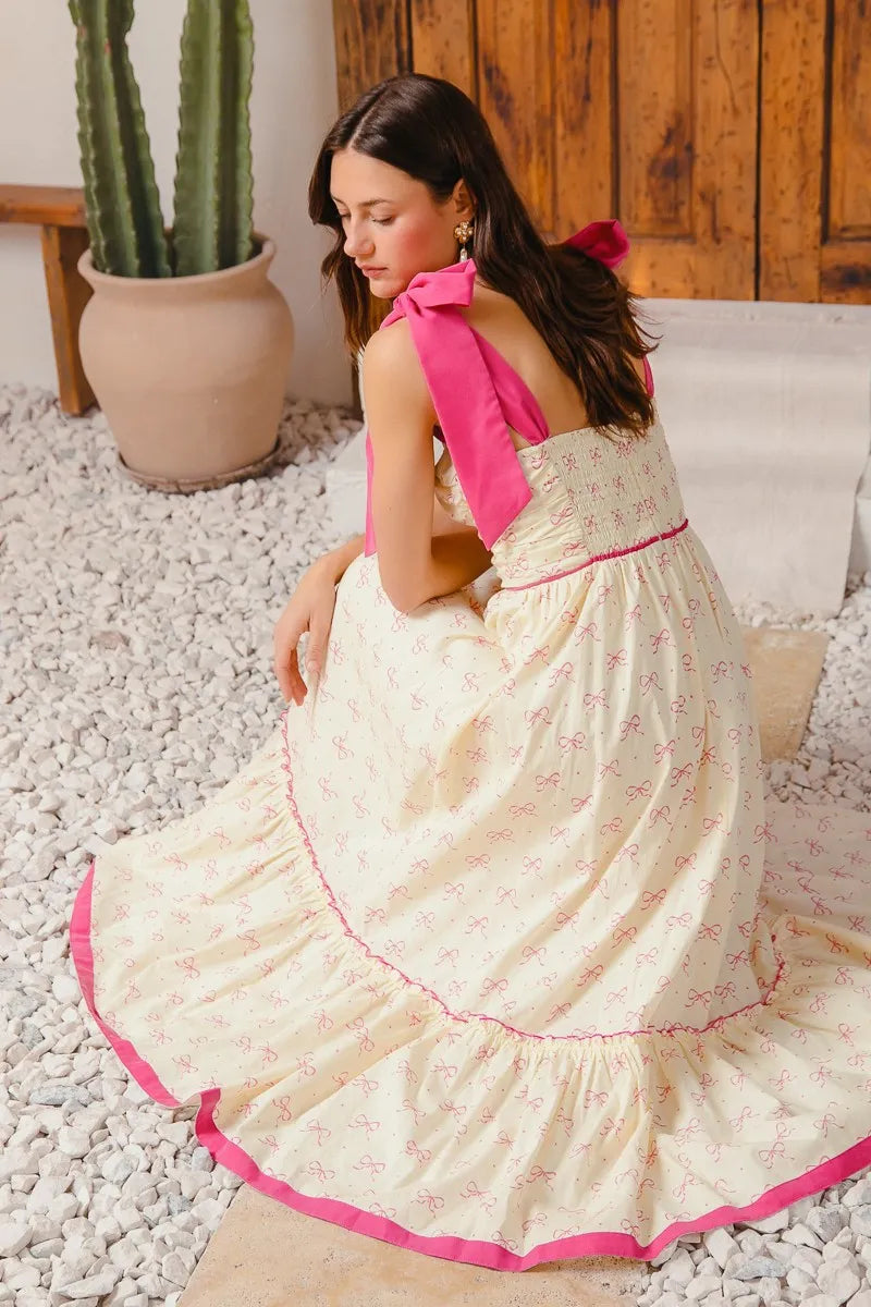 Sleeveless ribbon-print maxi in cream and hot pink with bow tie straps, tiered hem, elastic waist, smocked back and zipper.