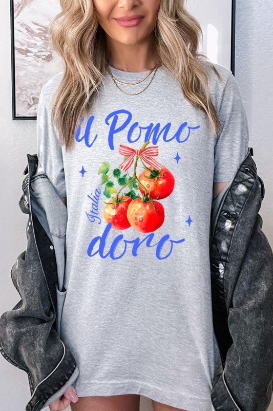 Model in a heather gray ‘Il Pomodoro’ tee, featuring a trio of glossy red tomatoes tied with a striped ribbon, framed by luxe blue script reading ‘Italia.’ Styled with soft, voluminous blonde waves and a draped noir jacket for a look that blends farmer’s market freshness with jet-set Mediterranean glamour.