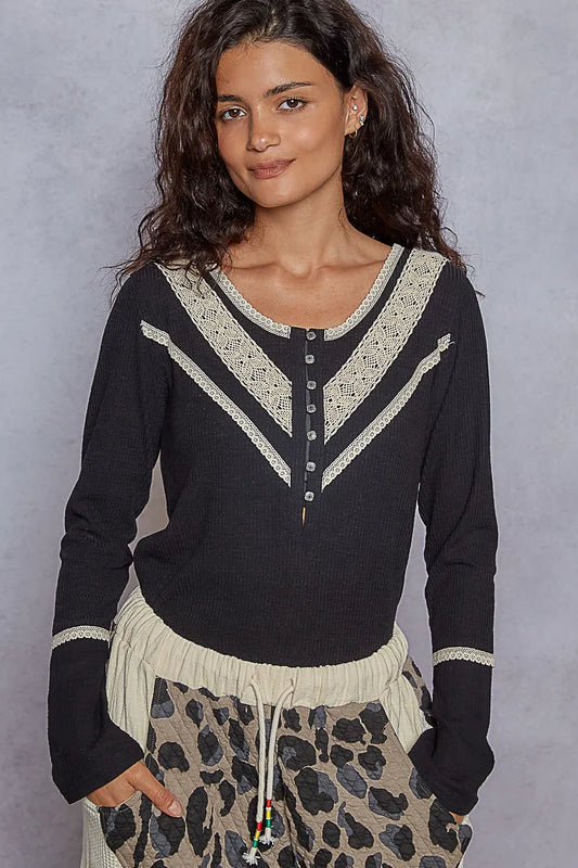 Black rib knit V-neck long sleeve top with half-button front and cream lace trim, worn with leopard print pants. Pictured on a plain background.
