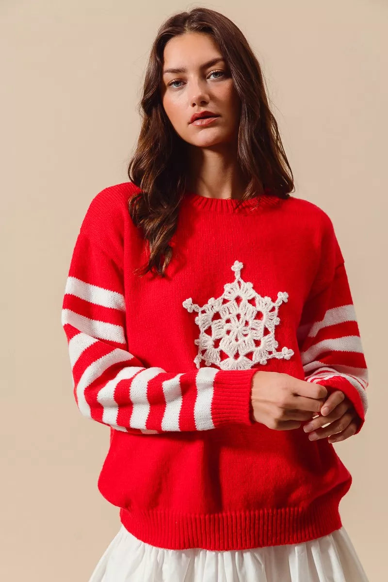 Red winter sweater featuring striped sleeves and crochet snowflake motif styled with skirt for casual layering