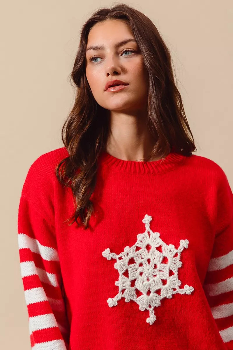 red knit sweater with white striped sleeve and crochet snowflake patch, close-up detail