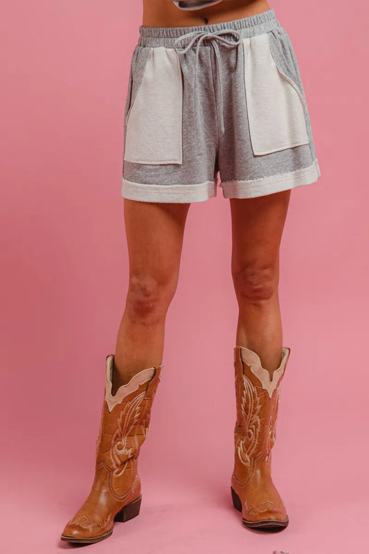 Woman in grey French terry lounge shorts with side pocket and cowboy boots, against pink backdrop – cozy summer style