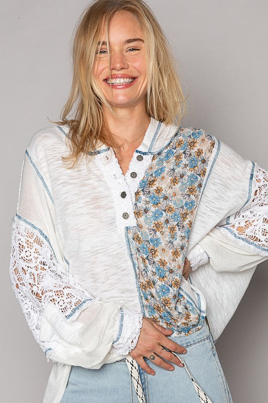 An oversized, loose fit, lightweight, ivory and blue floral hooded shirt. It’s predominately ivory slub knit with a blue floral pattern point detail panel on one half. It features a lace half button placket, long sleeves with crochet lace insets and a lace banded button cuffs. Bright Blue contrast stitching and flower shaped buttons complete the adorable, fresh and fun spring/summer hoodie top. 