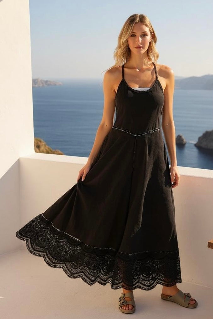 Model in black wide leg jumpsuit with lace trim, showcasing flowy fabric on a scenic coastal balcony.