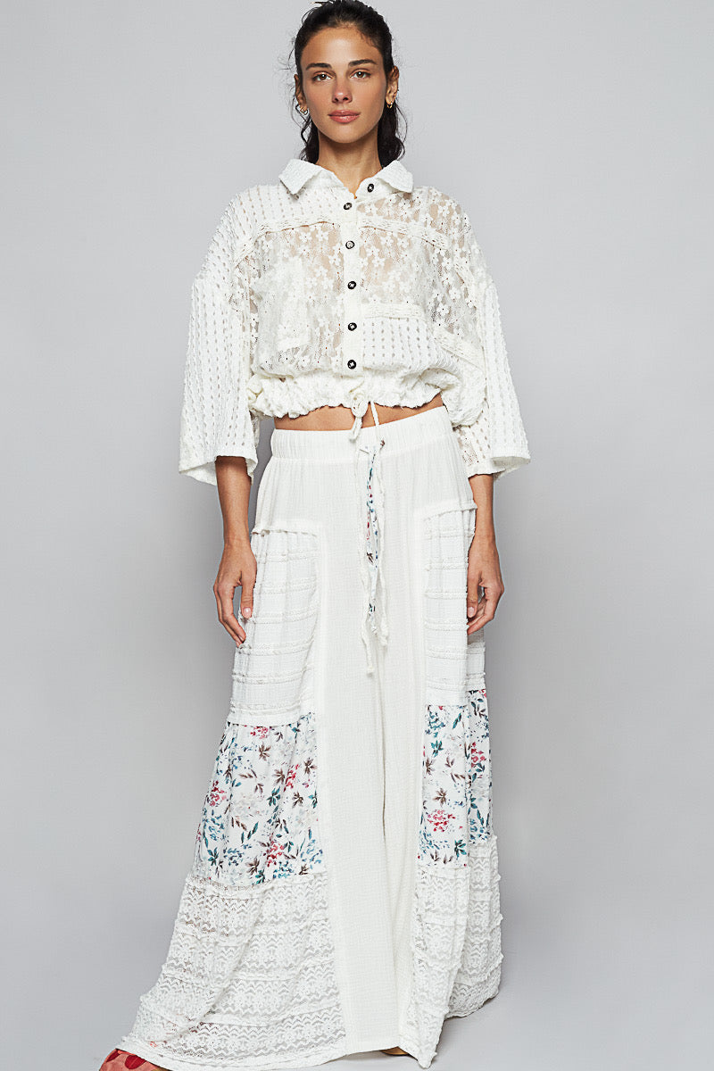 Studio shot of a woman wearing a white lace top and Sunspell Flares, showcasing the front view of the floral patchwork and lace panels, drawstring waist, and wide leg.