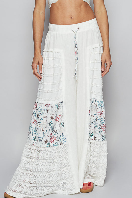 Studio shot of Sunspell Flares, displaying the elastic waistband, drawstring, front pockets, and intricate floral patchwork and lace panels on the wide legs.