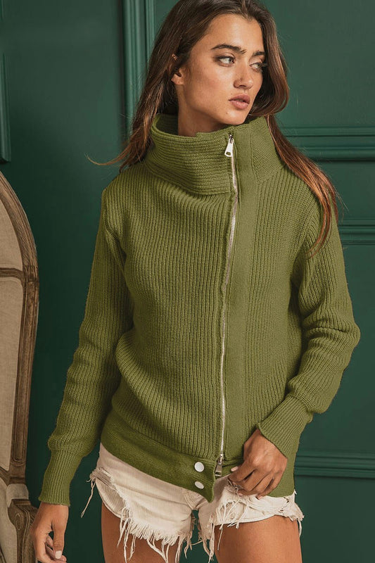 Olive rib knit long sleeve regular fit high-neck sweater with an off-center zipper and two bottom buttons, shown from the front and paired with cut-off shorts on a forest green paneled background.
