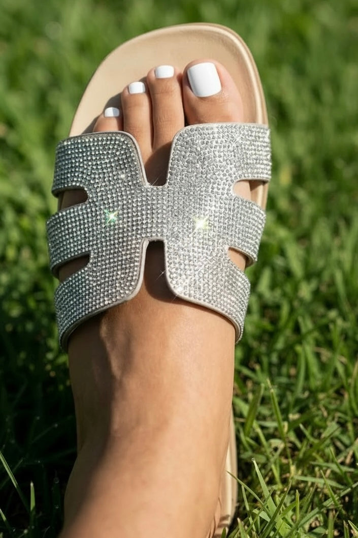 Slip on cruelty free sparkle sandal worn on foot in bright sunshine with a close up of the shimmering cutout single wide band