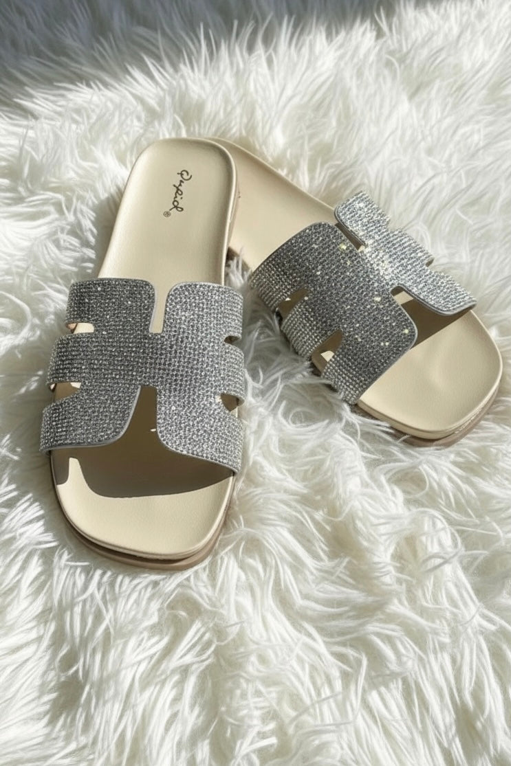 Sparkling crystal embellished open toe sandals with contoured footbeds diagonally on white faux fur rug in natural sunlight