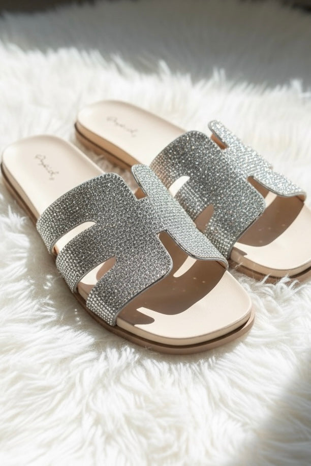 Silver crystal wide band sandals with a contoured beige footbed in natural light on white studio faux fur background