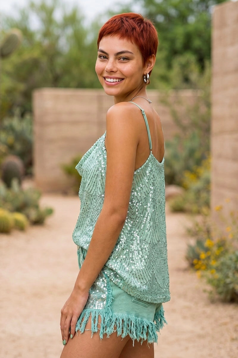 Mint sequin going out top with draped cowl neckline and thin straps, styled with fringe shorts in a desert garden