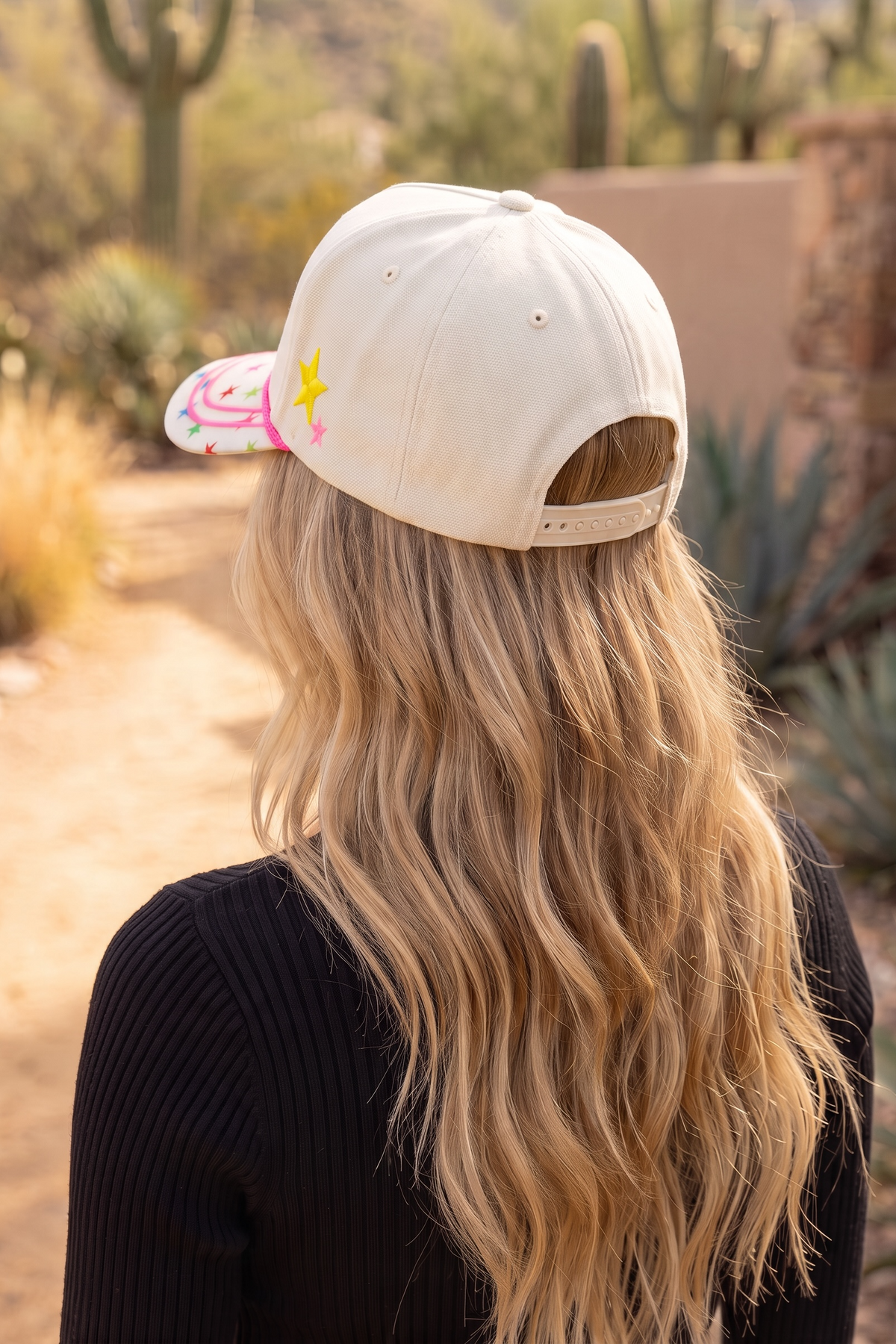 Adjustable snapback trucker hat in cream seen from behind with side stars in yellow and pink.