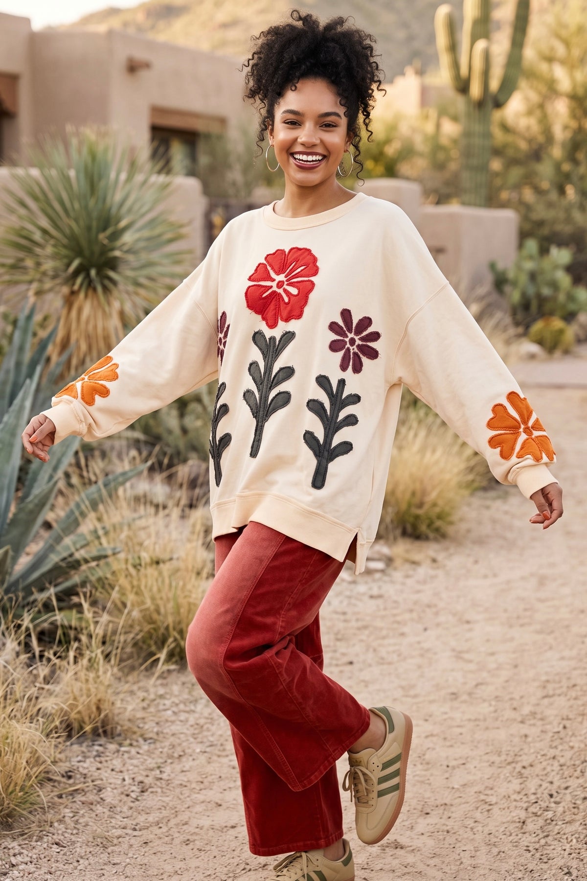 Ivory patchwork pullover with arms stretched wide showing red poppy patch and orange cuff flowers