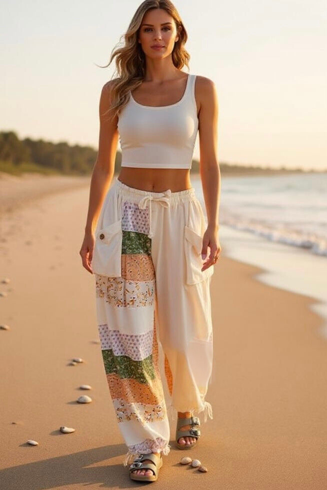 Model walking on a beach at sunset wearing the Shore Thing Pants in cream patchwork, showcasing the comfortable jogger style.