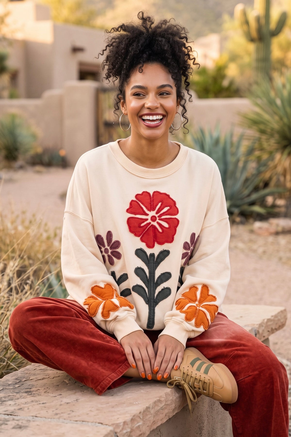 Flower applique pullover with terracotta sleeve blooms and ribbed crewneck seated on a stone ledge