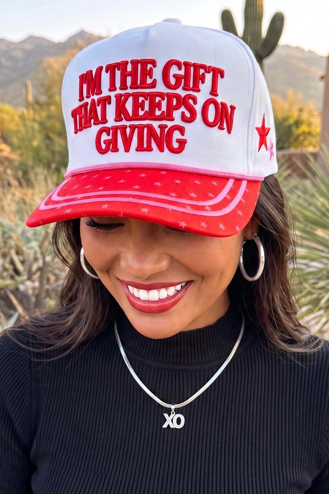 Christmas trucker hat with I'M THE GIFT lettering above a red star brim with two rows of pink stitching 