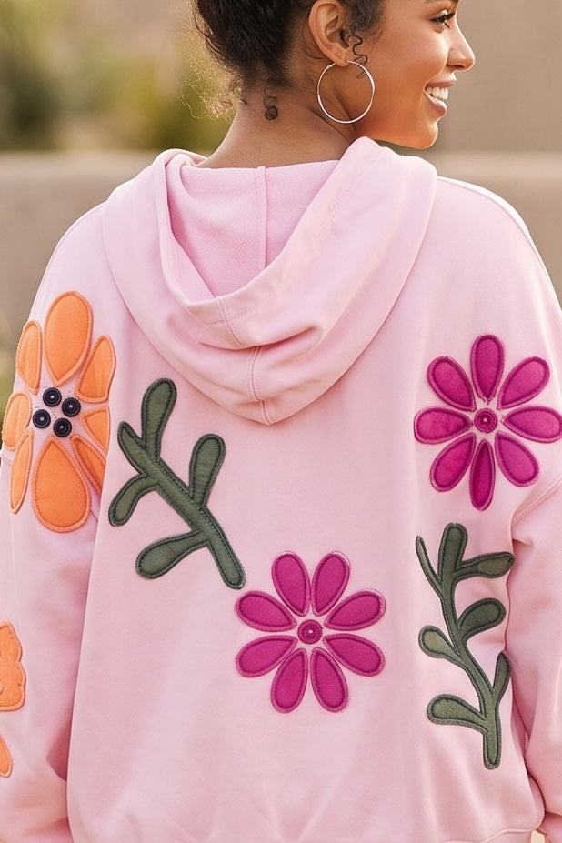 Pink hoodie showing large magenta and orange stitched flower appliqué patches with olive green stems
