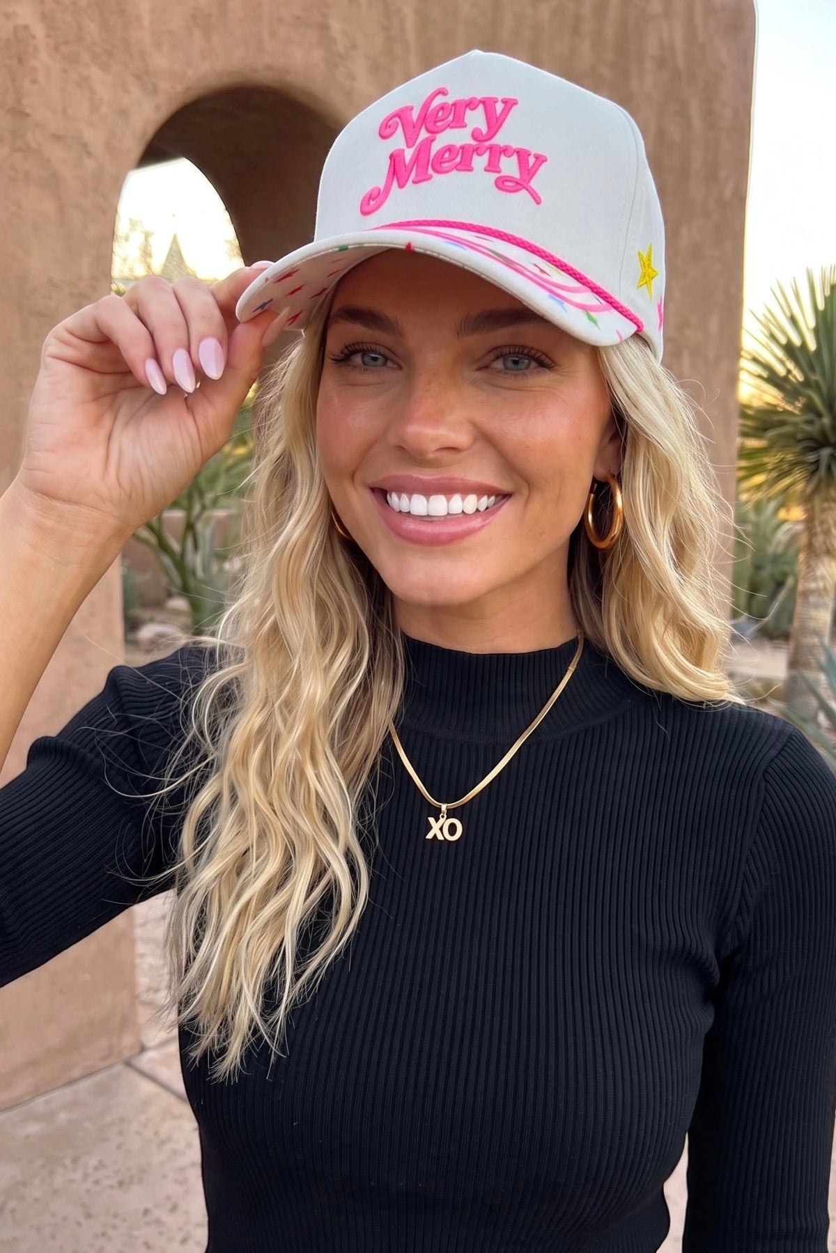 Festive Christmas cap with raised pink lettering and a star print brim held by two fingers.