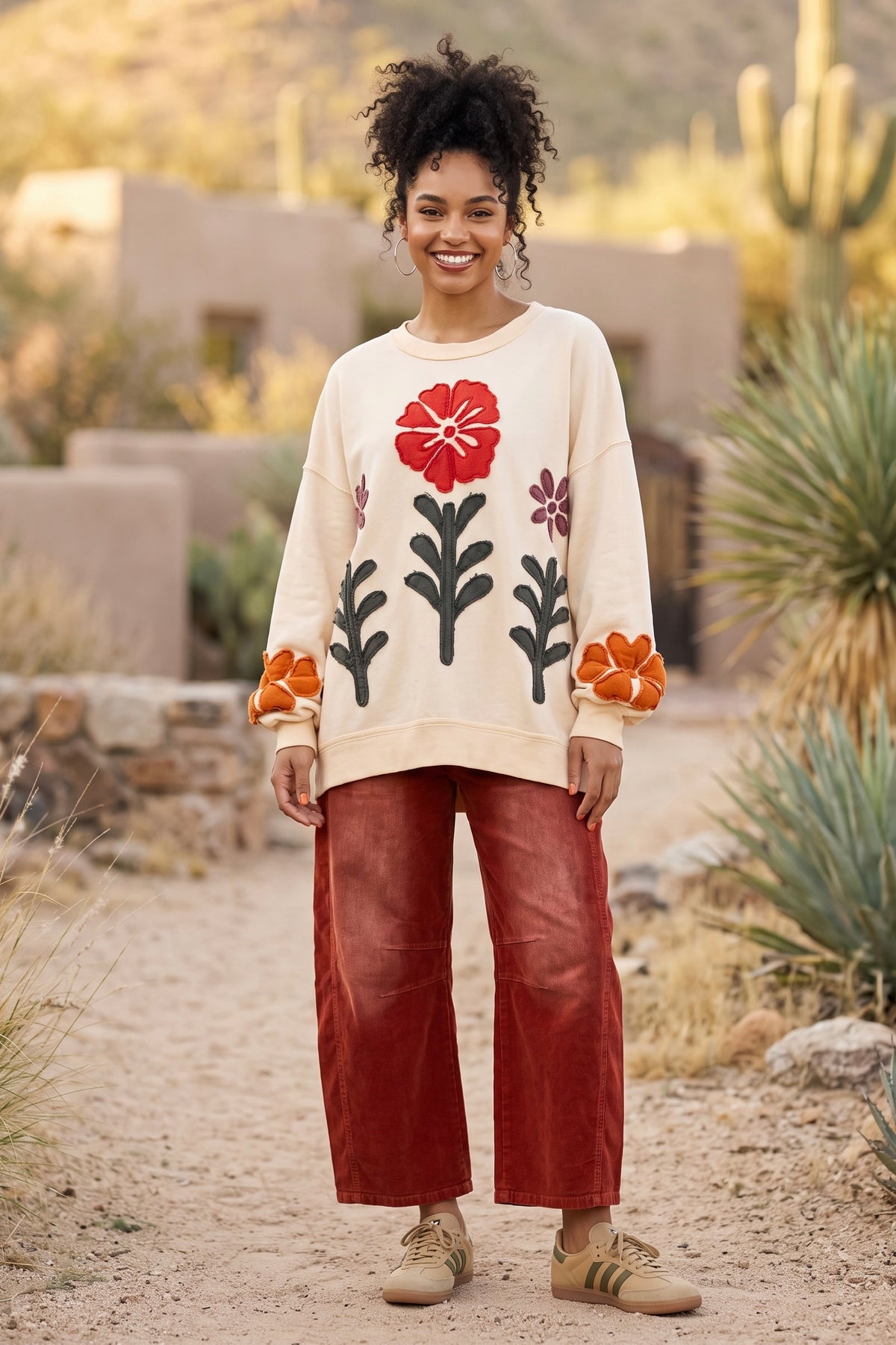 Floral applique pullover in ivory with red poppy and olive stems worn with rust pants outdoors