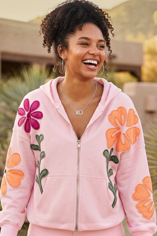 Pink zip up hoodie sweatshirt with bold orange and magenta floral appliqué patches on sleeves
