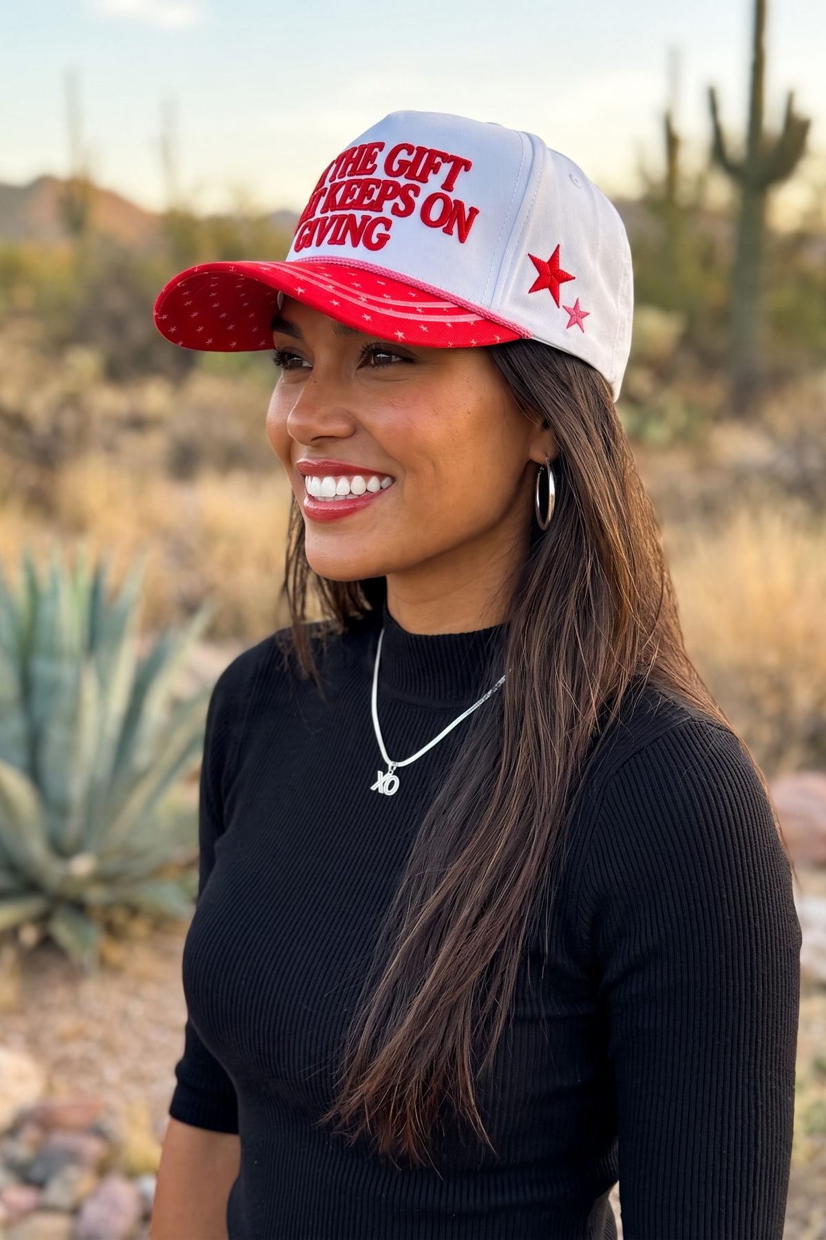 White embroidered statement holiday trucker hat with red lettering and red and pink side panel stars 