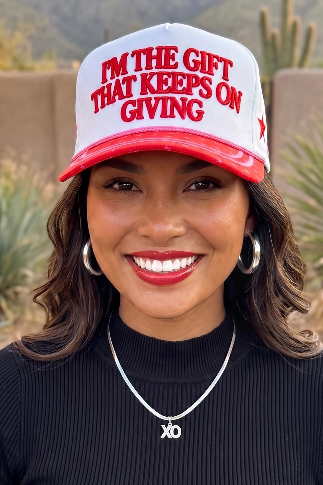 White trucker hat with 3D raised red embroidered I'M THE GIFT THAT KEEPS ON GIVING lettering.