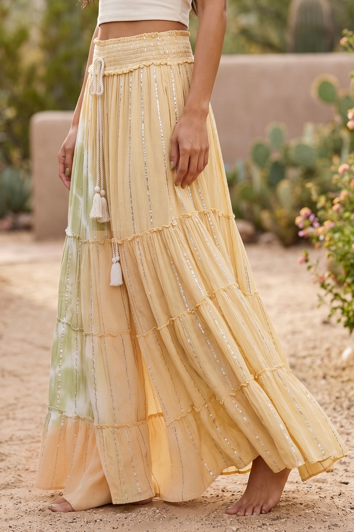 Pale yellow maxi skirt side view showing ruffled tier seams, twin tassels and shimmer stripes
